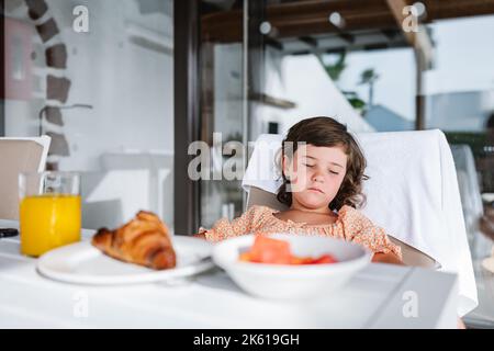 Selective focus of cute dark haired girl sleeping at table with food on plates in light cafeteria Stock Photo