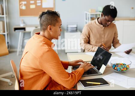 Side view portrait of creative black woman using laptop while working with team in meeting Stock Photo