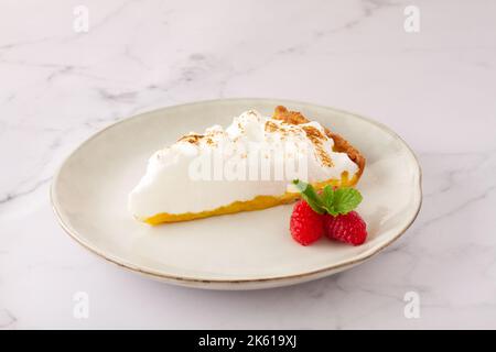 High angle of lemon meringue tart served on plate near ripe strawberries on marble table Stock Photo