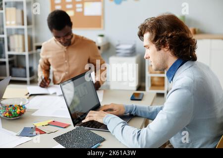 Side view portrait of Caucasian young man using laptop while working with team in meeting Stock Photo