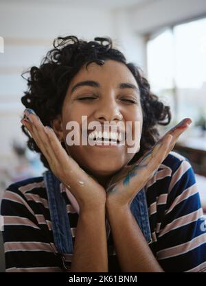 Woman artist, smile, happy and excited in her work studio, her hand with paint. Young painter, art and playful while working in workshop, painting and Stock Photo