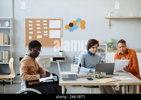 Side view portrait of black young man with disability working in office during diverse business team meeting Stock Photo