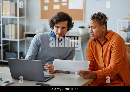 Portrait of two business people using laptop together while collaborating on project in minimal office setting Stock Photo
