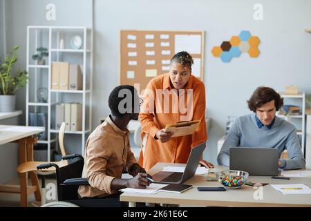 Side view portrait of black young man with disability listening to female manager in team meeting Stock Photo