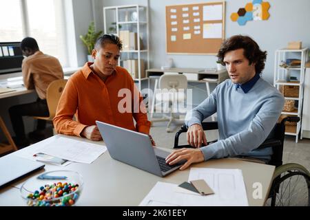 Portrait of Caucasian young man with disability presenting project to manager in accessible office setting Stock Photo