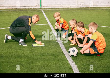 Junior soccer team training with football coach at sports stadium, outdoors. Concept of sport, competition, studying and achievements Stock Photo