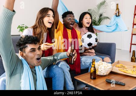 Diverse young football fans friends watching soccer on television TV at home Stock Photo