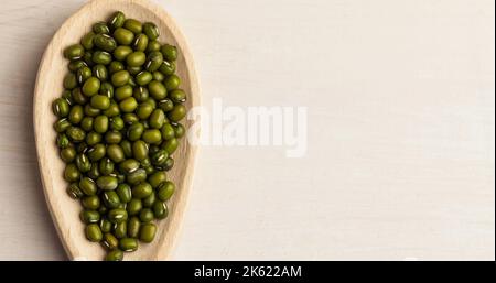 Directly above shot of green mung beans in wooden plate over white table, copy space Stock Photo