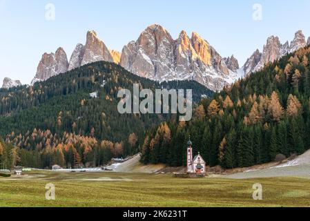 Autumnal sunset in the Dolomites. A lonely small church stands in the middle of a meadow at the foot of towering peaks. Stock Photo