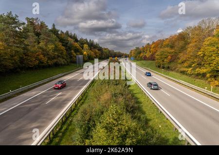 Cars are driving fast over a highway at the fall time, framed by beautiful trees, centred view. Stock Photo