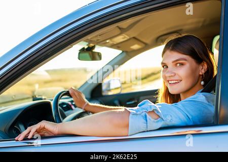 Beautiful happy smiling woman driving her new car at sunset Stock Photo