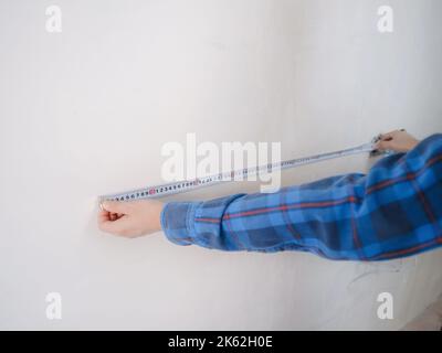Side view of serious man using measuring tape in room with underfloor heating pipes. Designer in shirt taking measurements while working on renovation Stock Photo