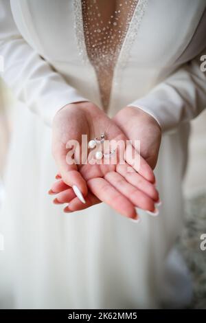 girl in a beautiful white dress holds earrings in her hands Stock Photo