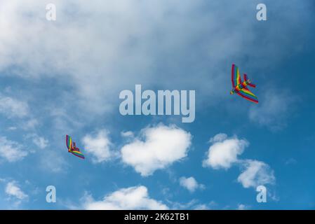 Two colorful kites in a blue sky with white clouds - focus on the kite in the foreground , Freedom and summer holiday concept Stock Photo