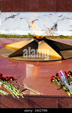 The eternal flame burns on a granite podium with flowers laid on it. Eternal memory to the fallen soldiers. Stock Photo