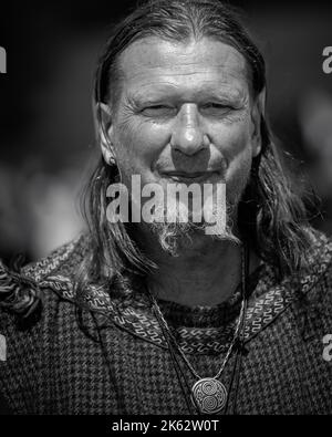 A vertical grayscale shot of a long-haired adult man wearing a medieval-styled jewelry Stock Photo