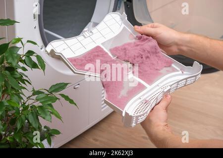 A man holds a dirty dryer filter. A man collects lint, hair, wool from the filter of a drying machine. Red lint on the dryer filter. Dirty filter dryer. Stock Photo