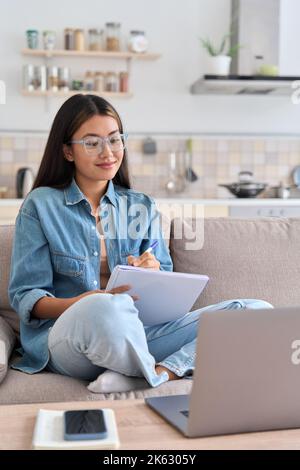 Teenager asian woman watching webinar on laptop making notes Stock Photo