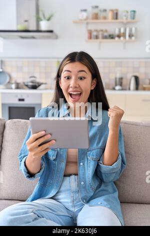 Excited asian woman celebrating success looking at digital tablet screen Stock Photo