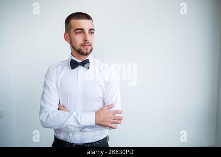 Young male businessman dressed in a white shirt with a short beard wears a black bow tie Stock Photo