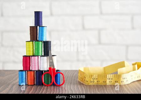 Pyramid of spools of multi-colored sewing threads, scissors, measuring tape on the table. Sewing production and hobby Stock Photo