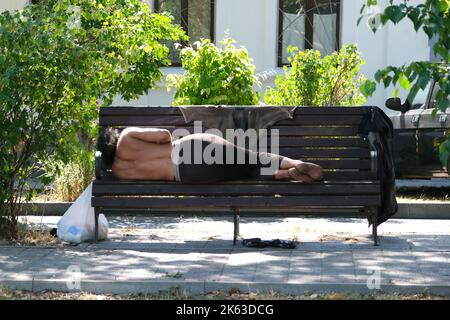 A homeless person takes a nap on a bench in a public park Stock Photo