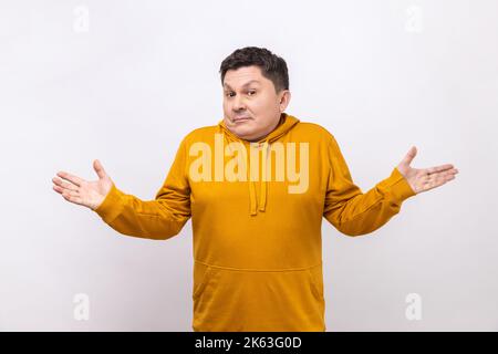 I don't know. Portrait of confused handsome young man standing with raised arms and dont know what to do, wearing urban style hoodie. Indoor studio shot isolated on white background. Stock Photo