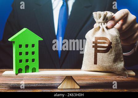 Businessman puts philippine peso money bag on scales and green house. Investment in renovation. Profitability housing of eco technologies. Reduced CO2 Stock Photo