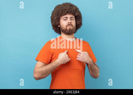 Portrait of man with Afro hairstyle drawing attention to itself, bragging with strength and endure, successful famous person posing at camera. Indoor studio shot isolated on blue background. Stock Photo