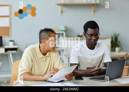 Portrait of two young people wearing casual clothes in office and using laptop together for work Stock Photo