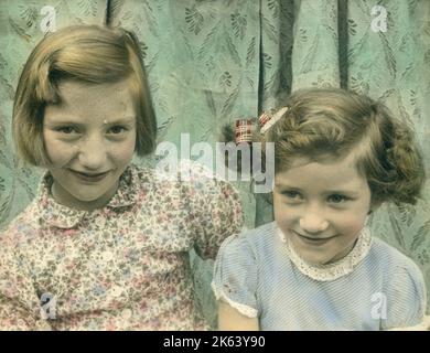 Delightful colour photograph of two little girls, possibly sisters, seated together.     Date: c.1950 Stock Photo