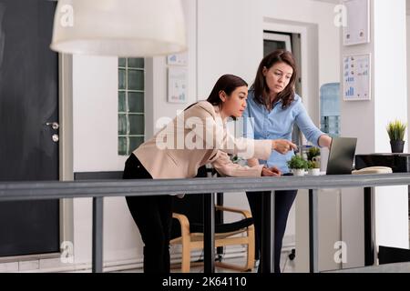 Employees collaboration, coworkers discussing company report in coworking space, woman pointing at computer screen. Workers chatting about strategy plan, standing in office Stock Photo