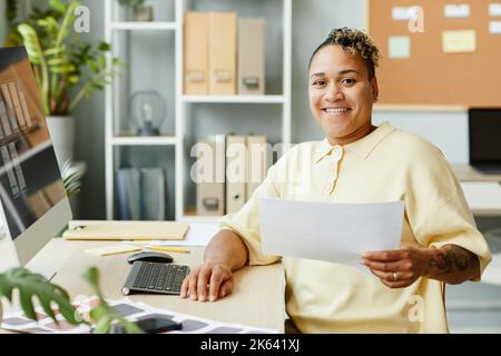 Portrait of tattooed black woman designing websites and mobile apps in office and smiling at camera Stock Photo