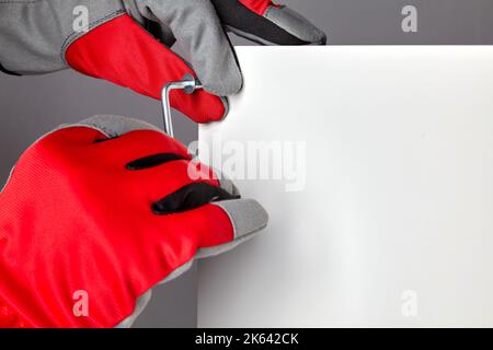 Hands in red gloves twist the confirmation with a hex key. Assembling new furniture with copy space Stock Photo