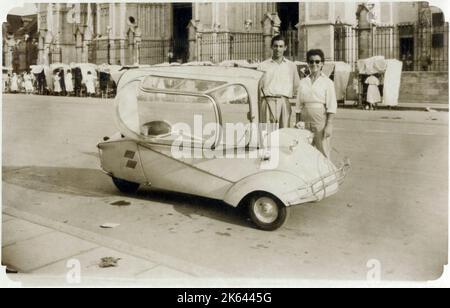 A young (possibly) Italian couple standing proudly next to their Messerschmitt KR200, or Kabinenroller (Cabin Scooter), a three-wheeled bubble car designed by the aircraft engineer Fritz Fend and produced in the factory of the German aircraft manufacturer Messerschmitt from 1955 to 1964. Stock Photo