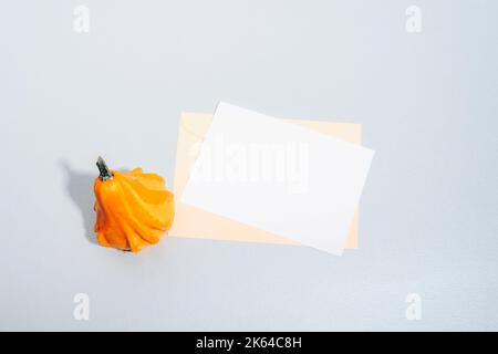 Orange decorative pumpkin and envelope with blank sheet on gray background. Autumn holidays concept. Top view, flat lay, mockup Stock Photo