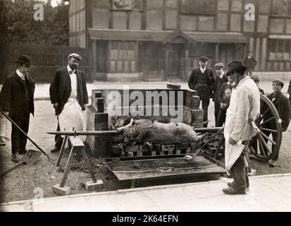Early 20th century vintage press photograph - men roasting a pig on a spit in the street, somewhere in the UK  c.1920s Stock Photo