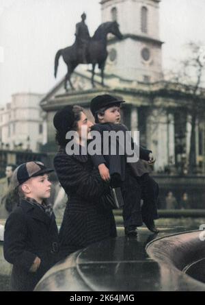 A delightful photograph of a Mother and her two boys by one of the fountains in Trafalgar Square, London - 1950s. The distinctive shape of the Church of St Martin-in-the-Fields can be seen in the background, behind the statue of King George IV on horseback. Stock Photo