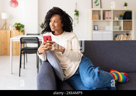 Smiling young brazilian woman holding mobile phone while relaxing on sofa Stock Photo