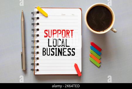 Support local business text written on a notepad on a table with a cup of coffee, glasses and a pen, in sunlight. Business concept Stock Photo