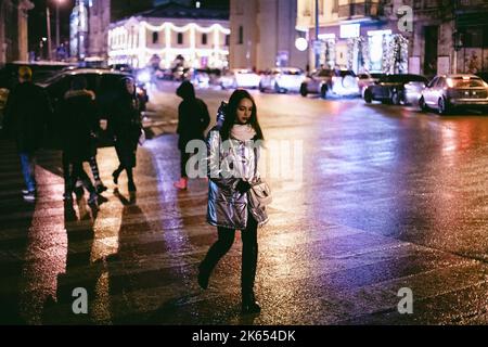 Young woman crossing road in city during winter at night Stock Photo