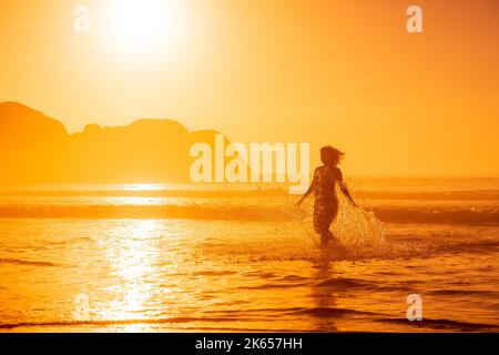 Pregnant woman walking on ocean beach at beach with sunrise or sunset tones Stock Photo
