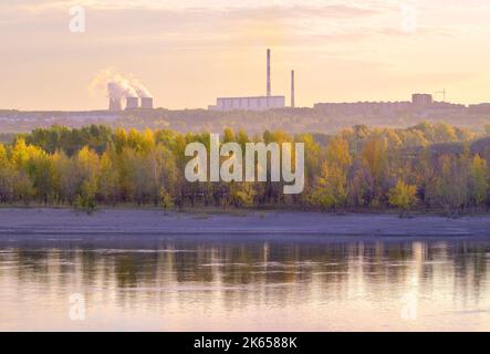 The Ob coast in the morning. Autumn forest by the river, CHP-5 pipes on the horizon. Novosibirsk, Siberia, Russia, 2022 Stock Photo