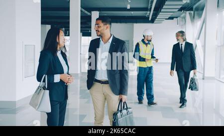 Diverse group of businesspeople are talking to worker in uniform inside industrial buiding checking papers discussing project. People and business concept. Stock Photo