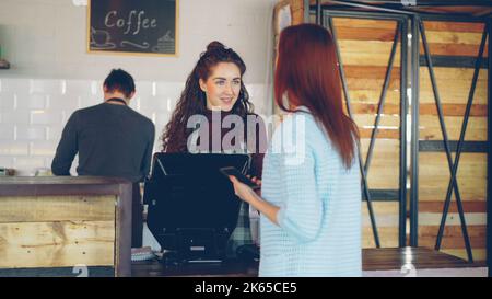 Young female customer purchasing takeout coffee in modern coffee shop. Stock Photo