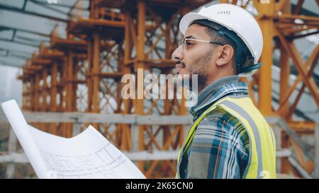 Portrait of engineer planning work at construction site looking at blueprint outdoors in industrial zone. People and occupation concept. Stock Photo