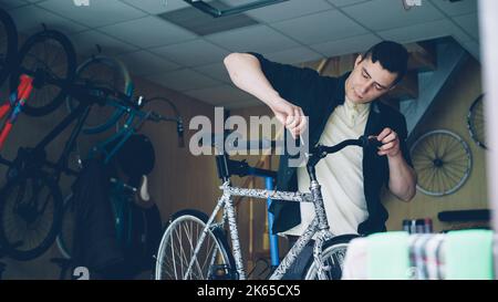 Skilled mechanic is fixing handle-bar of modern bicycle using professional tools in workshop with spare parts and equipment. Bike maintenance and repair and people concept. Stock Photo