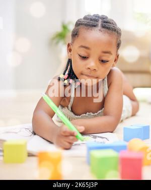 This is going to be my best picture yet. an adorable little girl lying on the living room floor alone and colouring. Stock Photo