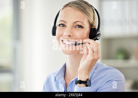 Portrait of young caucasian female call centre agent talking on headset while working on computer in an office. Confident and happy businesswoman Stock Photo
