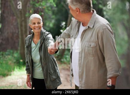 A mature couple holding hands while out hiking together. Senior couple smiling during a hike looking happy in nature Stock Photo